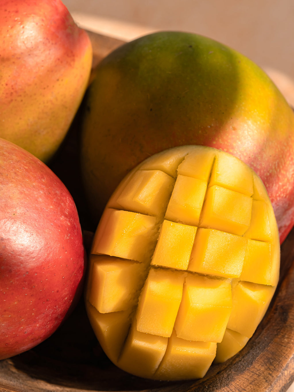 Mangoes with a sliced mango on a wooden surface
